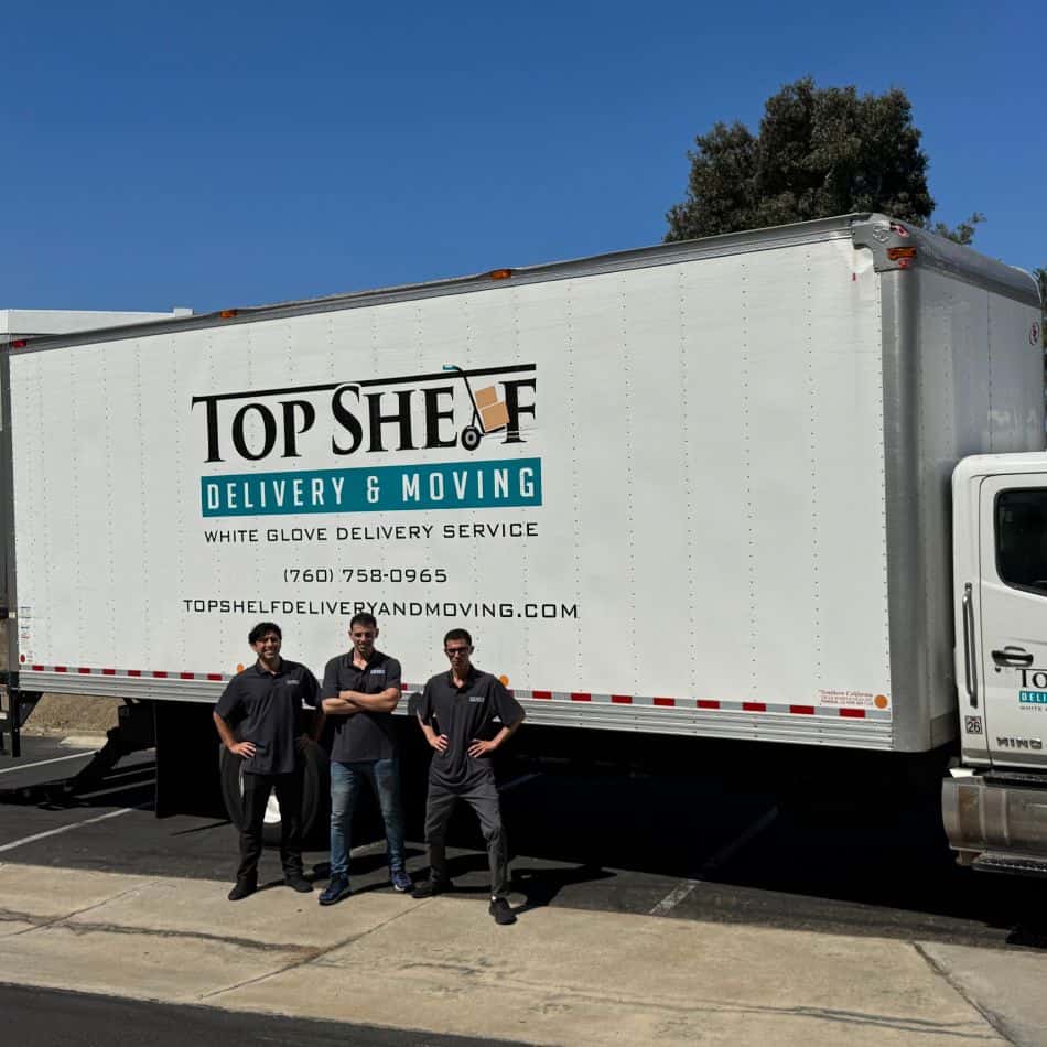 Three professional Top Shelf movers standing confidently in front of a white glove delivery truck.