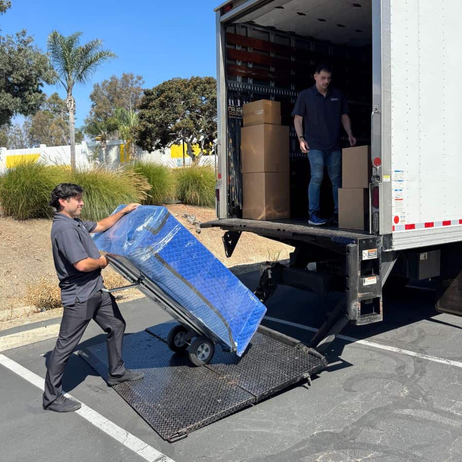 Professional mover using a heavy-duty dolly to load a blue-wrapped furniture item into a Top Shelf moving truck.
