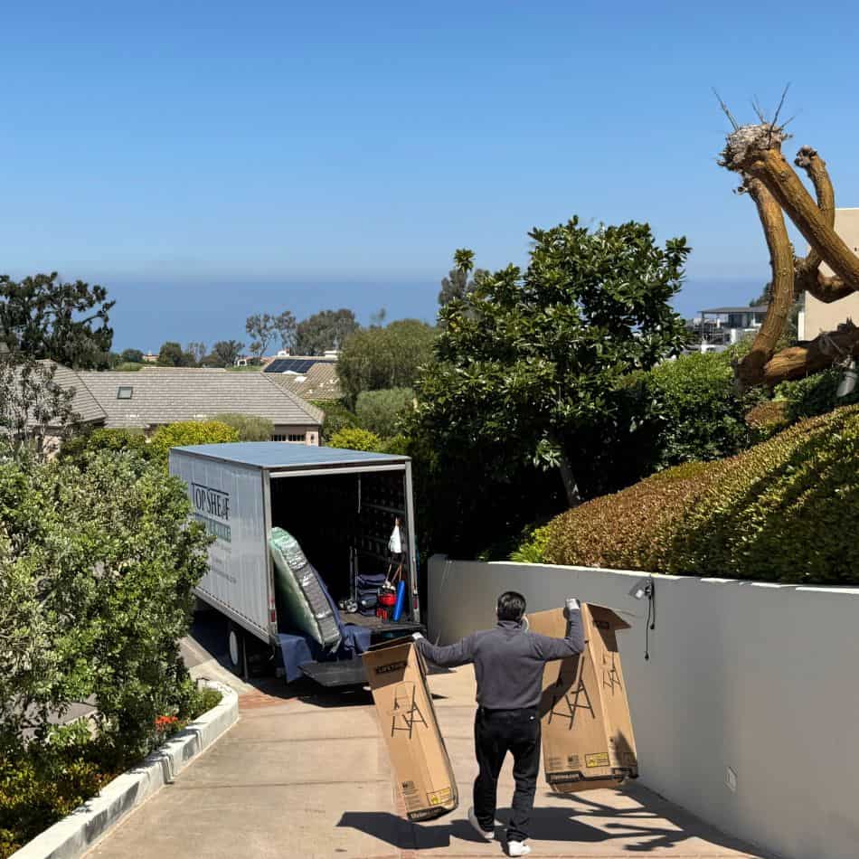 Professional mover carefully loading protected furniture into a Top Shelf moving truck on a steep residential driveway.