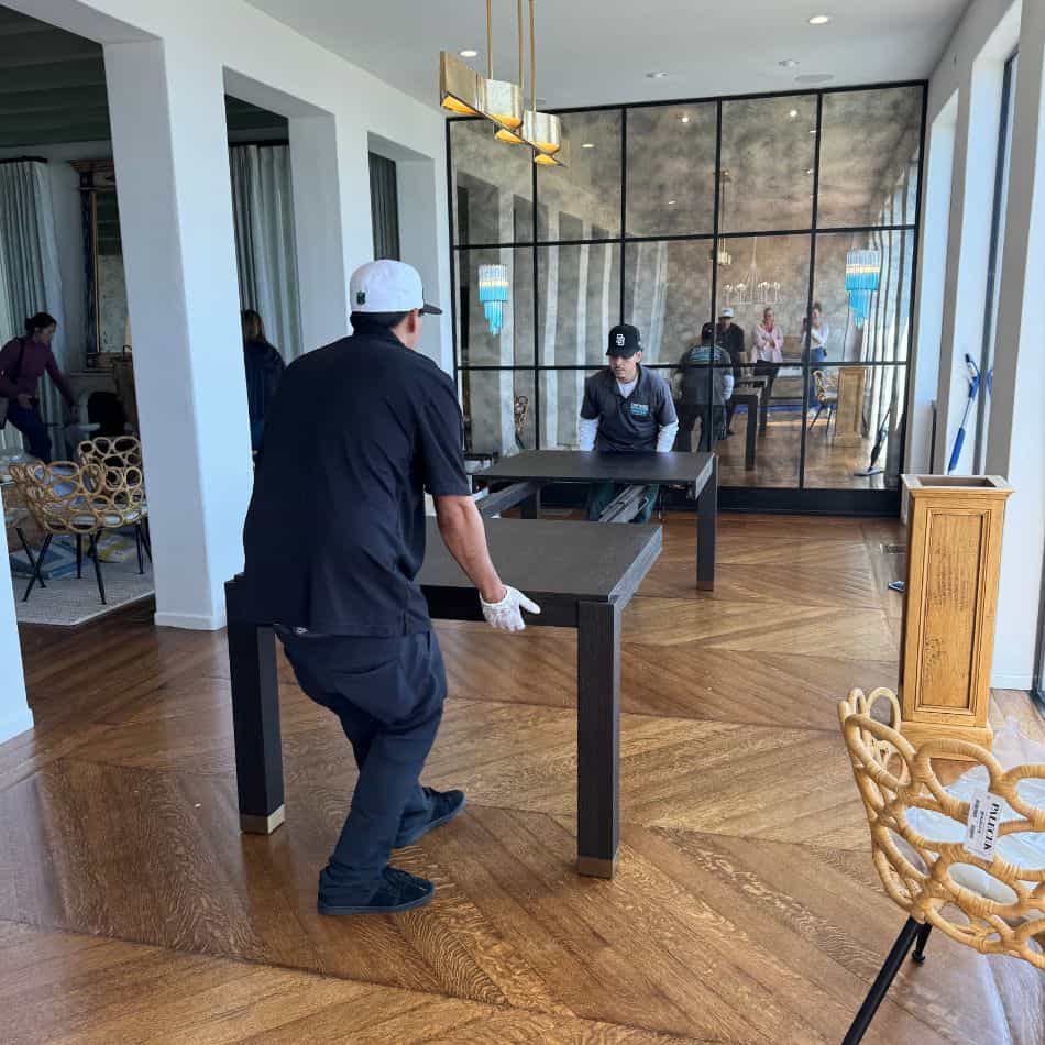 Expert white glove movers in gloves meticulously assembling a large dark wood dining table in a luxury home.
